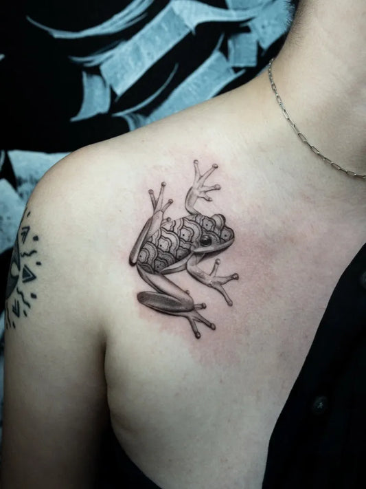 Small Black and Grey Frog Tattoo on Women Shoulder by @ikonikinktattoo