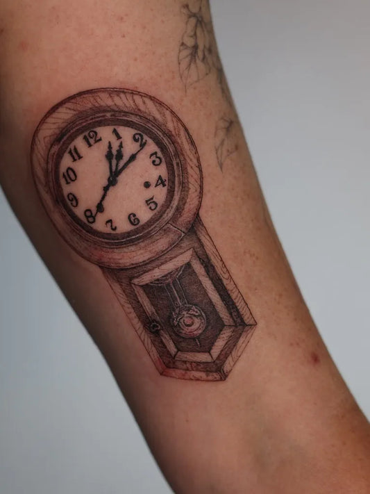 Small Black and Grey Grandfather Clock Tattoo on Women Arm by @addy.tattoo