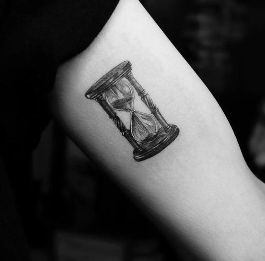 Small Black and Grey Hourglass Tattoo on Women Upper Arm by @fridaystattoohk