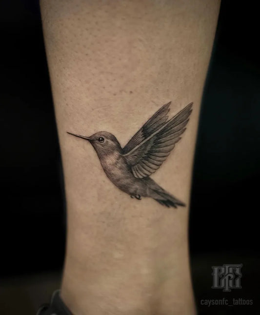 Small Black and Grey Hummingbird on Women Leg Tattoo by @caysonfc_tattoos