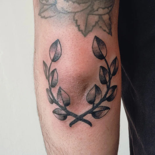 Small Black and Grey Laurel Wreath Tattoo on Men Knee by @philip.anthony_