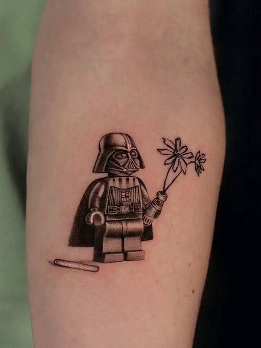 Small Black and Grey Lego Darth Vader with Flowers Tattoo on Women Forearm by @ruth.tatts