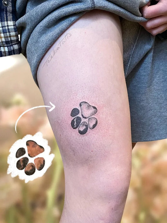 Small Black and Grey Paw Print Tattoo on Women Thigh by @teekatatts