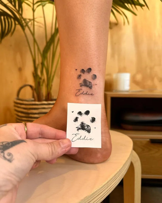 Small Black and Grey Paw Print and Name Tattoo on Women Ankle by @inkypalette.tat