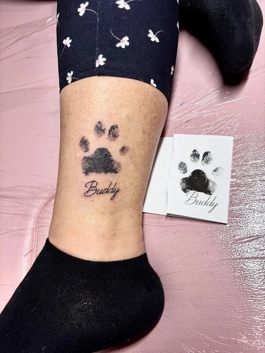 Small Black and Grey Paw Print with Buddy Name Tattoo on Women Ankle by @tattoosam.k