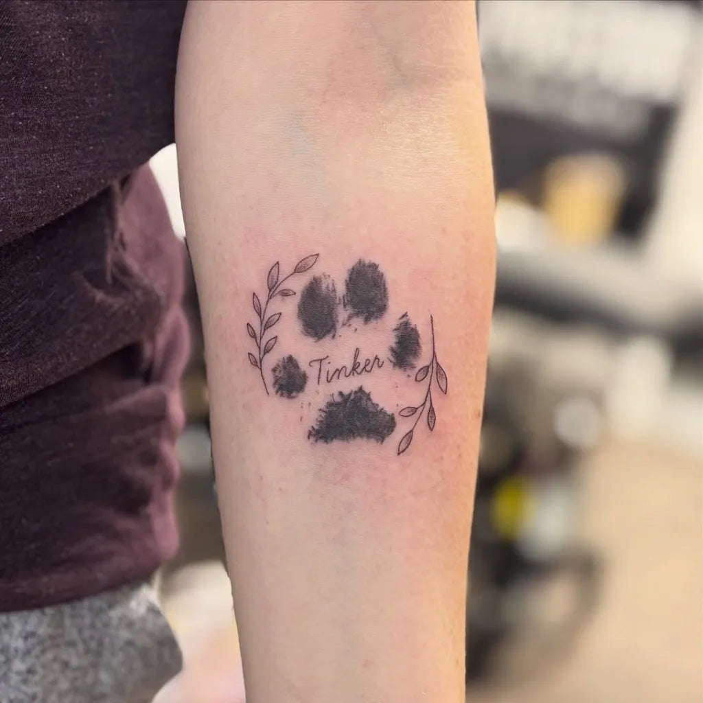 Small Black and Grey Paw Print with Wreath and Name Tattoo on Women Arm by @ironrextattoo