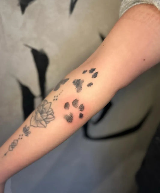 Small Black and Grey Paw Prints and Lotus Tattoo on Women Forearm by @saishamaytattoos