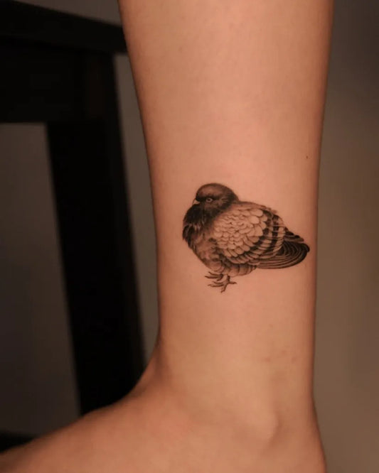 Small Black and Grey Pigeon Tattoo on Women Ankle by @kamilarthurtattoo