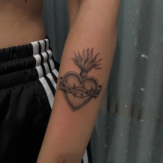 Small Black and Grey Sacred Heart with Crown of Thorns and Flames Tattoo on Women Arm by @macarthur.tattoos