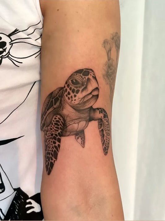 Small Black and Grey Sea Turtle Tattoo on Women Arm by @emiliehuottattoo_officiel