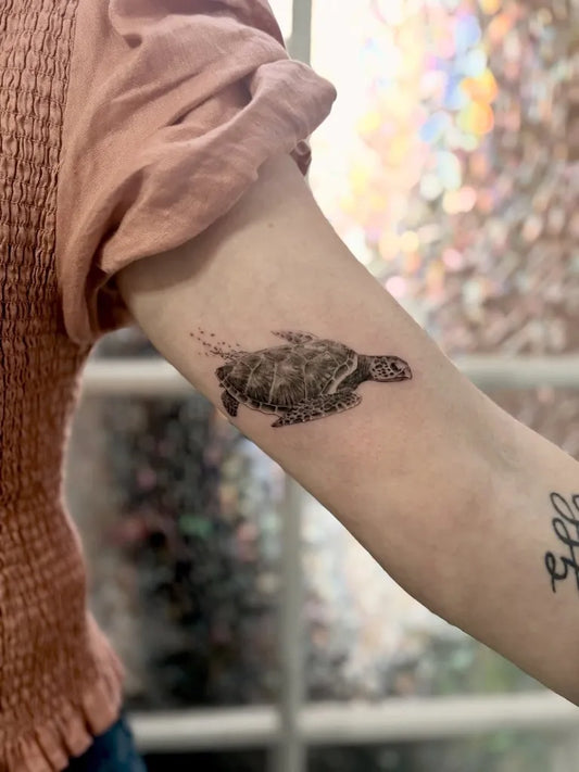 Small Black and Grey Sea Turtle Tattoo on Women Upper Arm by @guysvl