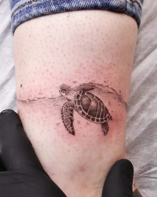 Small Black and Grey Sea Turtle and Wave Tattoo on Women Leg by @eggsy_tattoo