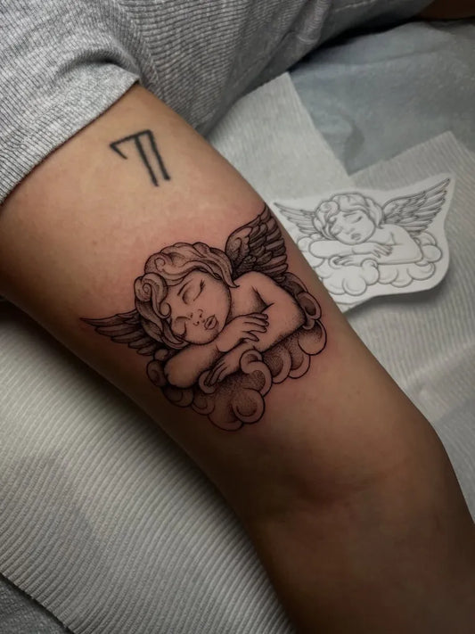 Small Black and Grey Sleeping Angel with Wings on Women Arm Tattoo by @msbeetattoos
