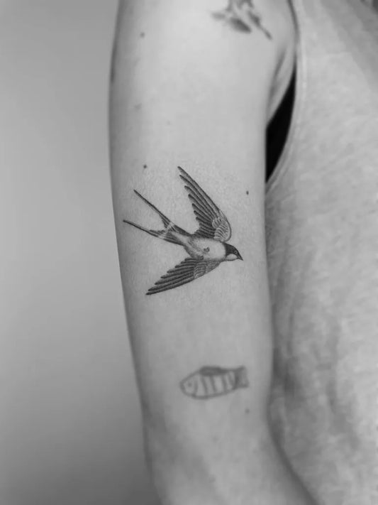 Small Black and Grey Sparrow and Fish Tattoo on Women Upper Arm by @fantasyandfuntattoo