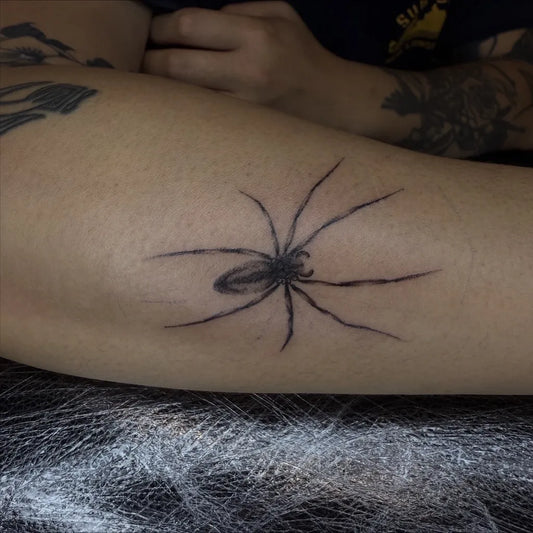 Small Black and Grey Spider on Women Thigh Tattoo by @macarthur.tattoos