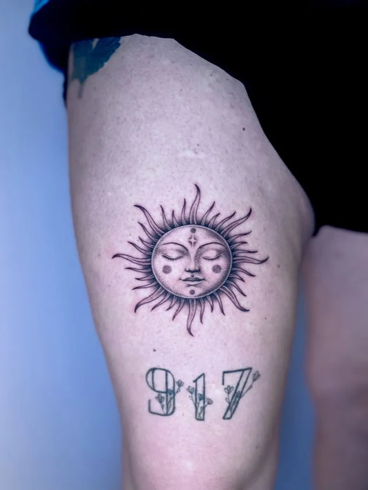 Small Black and Grey Sun with Face and Date on Women Thigh Tattoo by @leahtattoos