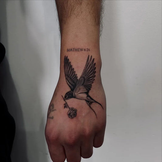 Small Black and Grey Swallow with Rose Tattoo on Men Wrist by @blankspot.ink