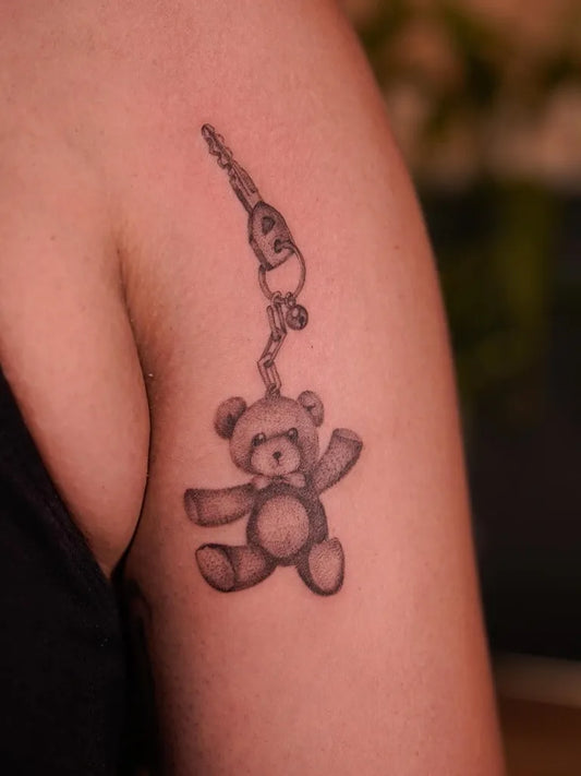 Small Black and Grey Teddy Bear Keychain on Women Upper Arm Tattoo by @nickilyen