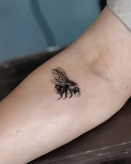 Small Blackwork Bee on Women Arm Tattoo by @piranhatattoostudios