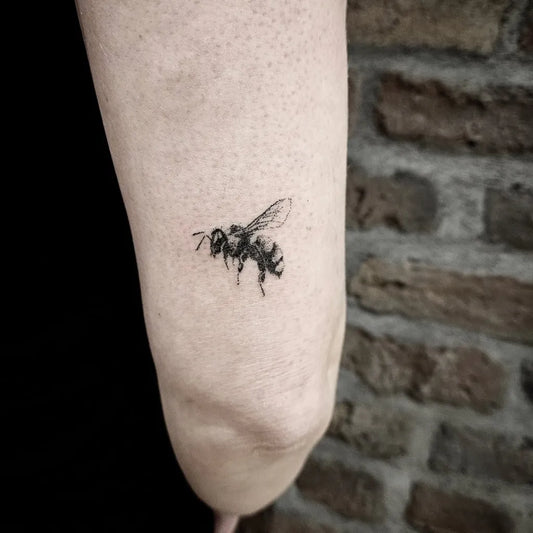 Small Blackwork Bee on Women Elbow Tattoo by @tins.handpoke