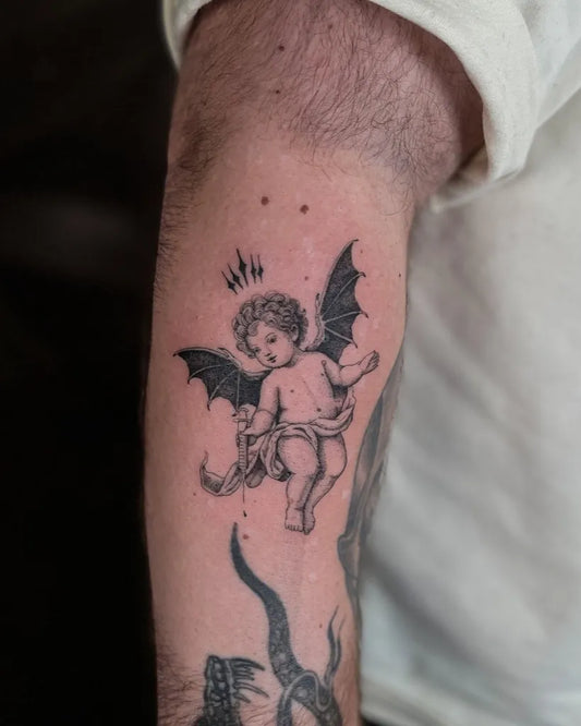 Small Blackwork Cherub with Bat Wings Tattoo on Men Arm by @ironsideink