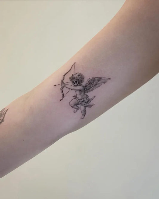 Small Blackwork Cherub with Bow Tattoo on Women Arm by @johnb.designs