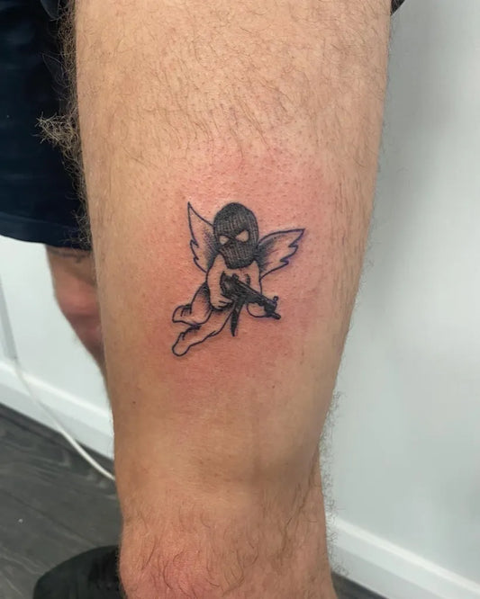 Small Blackwork Cherub with Mask and Rifle Tattoo on Men Thigh by @sam_small_ink_