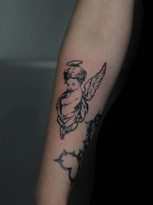 Small Blackwork Cherub with Thorns Tattoo on Women Arm by @m_juziuk_tattoo