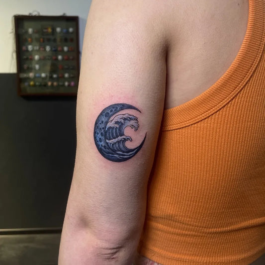 Small Blackwork Crescent Moon and Wave Tattoo on Women Upper Arm by @dex_ter_tattoo