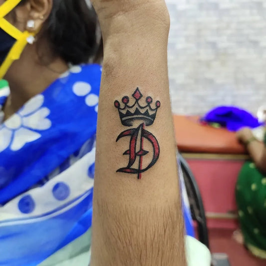 Small Blackwork Crown and D Letter Tattoo on Men Wrist by @angel_tattoo_studio__