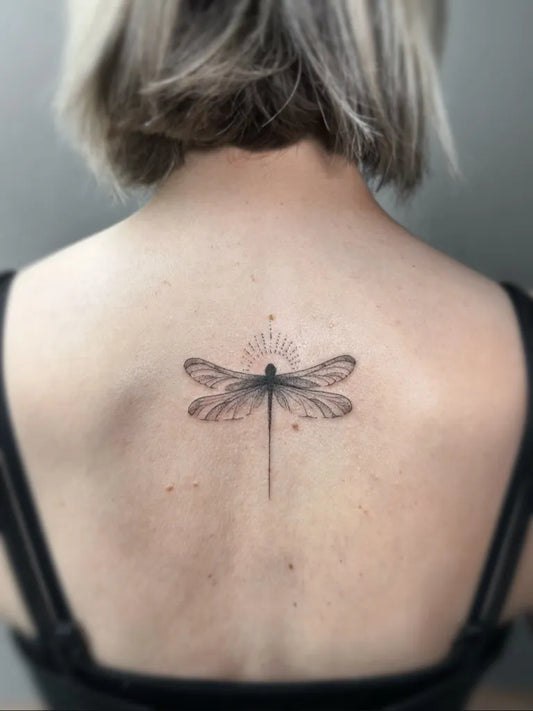 Small Blackwork Dragonfly with Sunburst on Women Back Tattoo by @finelinetattooslondon