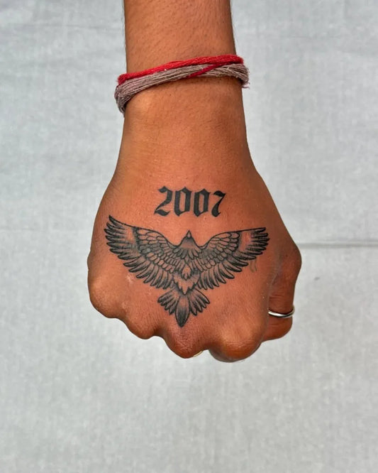 Small Blackwork Eagle with Date Tattoo on Women Hand by @the_tattoo_club_78