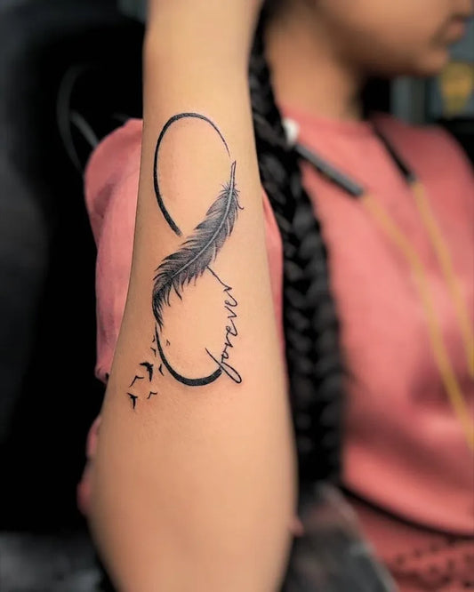 Small Blackwork Feather Infinity Tattoo on Women Arm by @nirvanatattooandarts