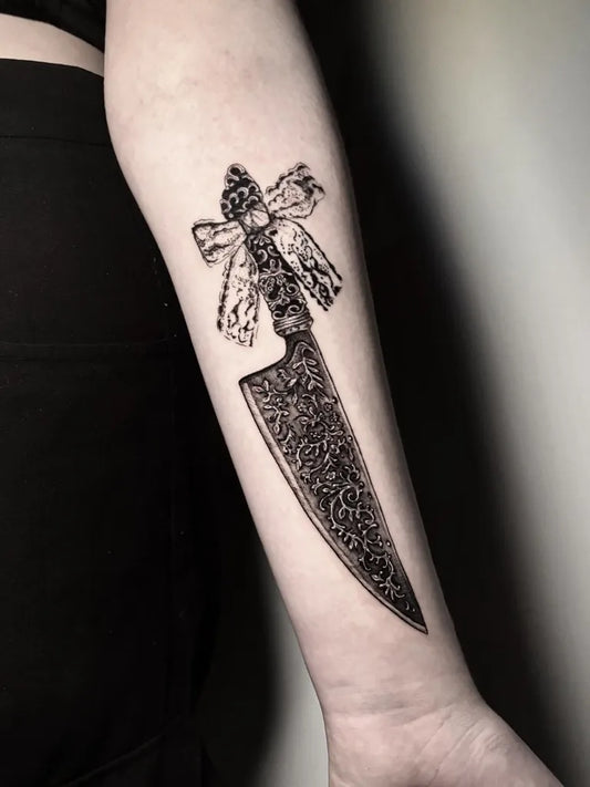 Small Blackwork Knife and Bow Tattoo on Women Arm by @weirdgirltattoo