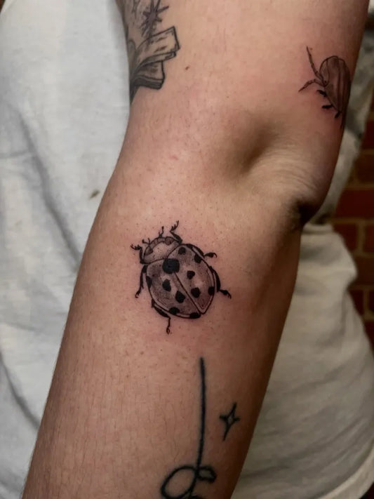 Small Blackwork Ladybug Tattoo on Women Arm by @obscura.tattoo