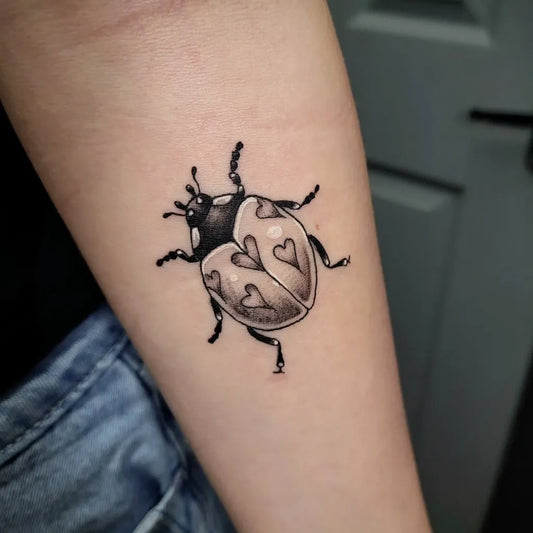 Small Blackwork Ladybug with Hearts Tattoo on Women Arm by @gingersnapped.tatts