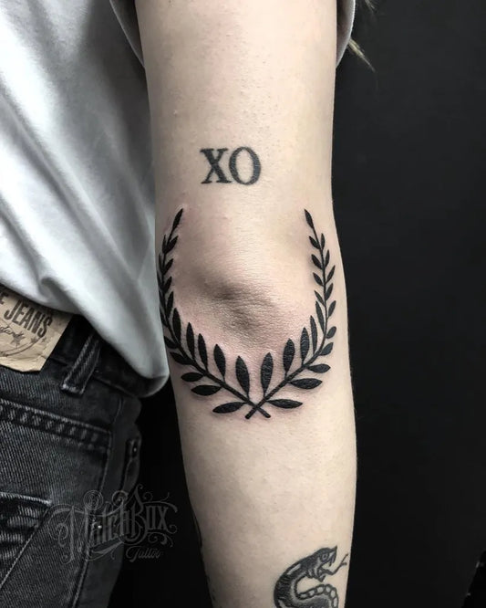 Small Blackwork Laurel Wreath XOTattoo on Women Elbow by @matchboxtattoo