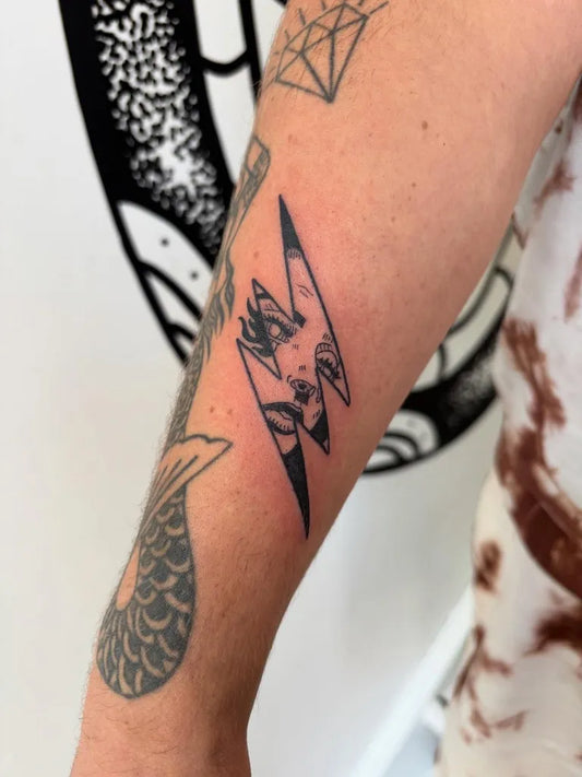 Small Blackwork Lightning Bolt with Face Tattoo on Women Arm by @tamartielemantattoo