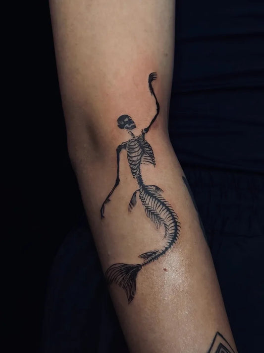 Small Blackwork Mermaid Skeleton Tattoo on Women Arm by @mahla.inkk