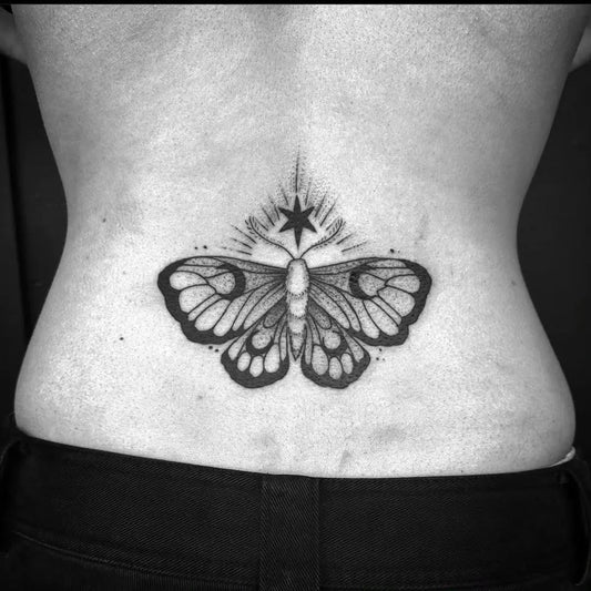 Small Blackwork Moth with Star Tattoo on Women Lower Back by @echelontattoo