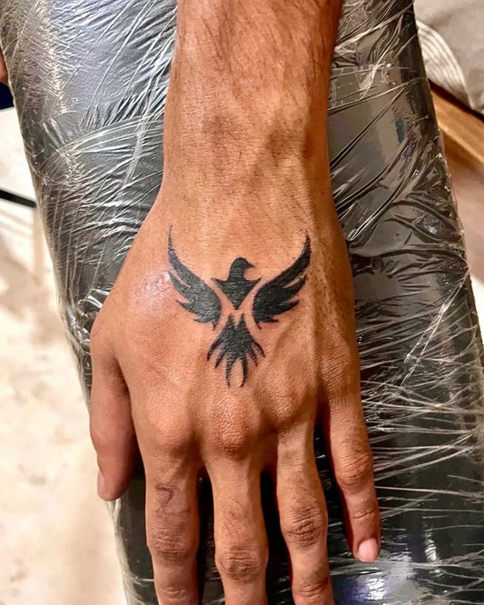 Small Blackwork Phoenix with M Flame on Men Hand Tattoo by @jiten.arora