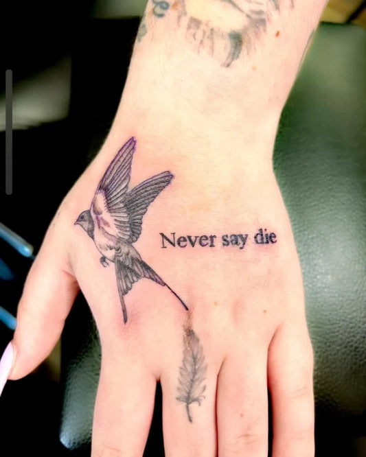 Small Blackwork Swallow Feather Never Say Die Tattoo on Women Hand by @indi_tattoos
