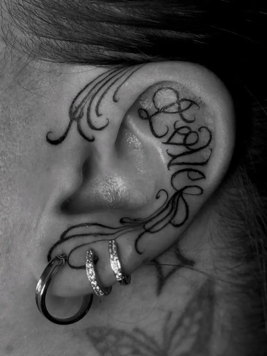 Small Blackwork Word and Flourish Tattoo on Women Behind the Ear by @lauramayartist