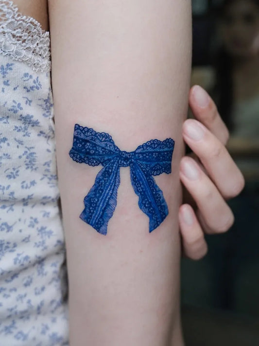 Small Blue Lace Bow Tattoo on Women Arm by @standforsea.yc