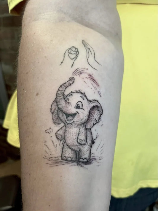 Small Cartoon Elephant with Hands Tattoo on Women Arm by @jochastney.tattoo