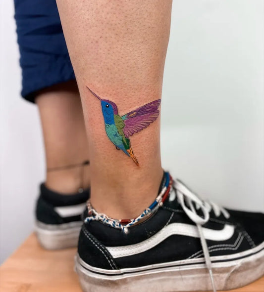 Small Colorful Hummingbird Tattoo on Women Leg by @burcuerimtatt