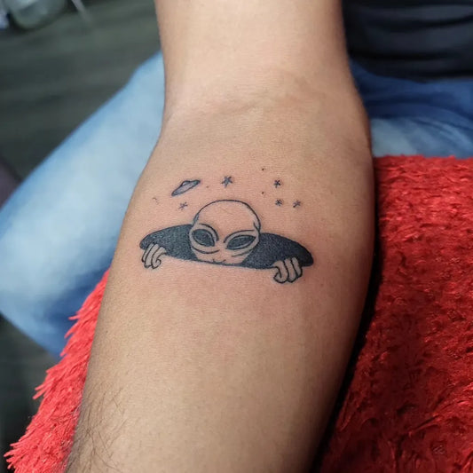 Small Fine Line Alien Peeking Out Tattoo on Men Forearm by @arthanaari_inks
