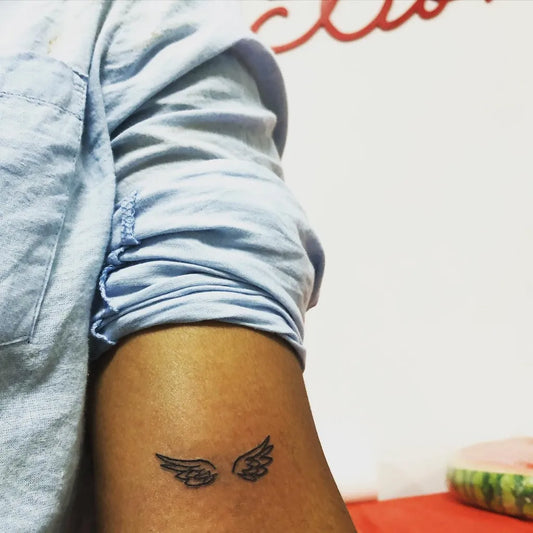 Small Fine Line Angel Wings Tattoo on Women Arm by @inkjectiontattoostudio