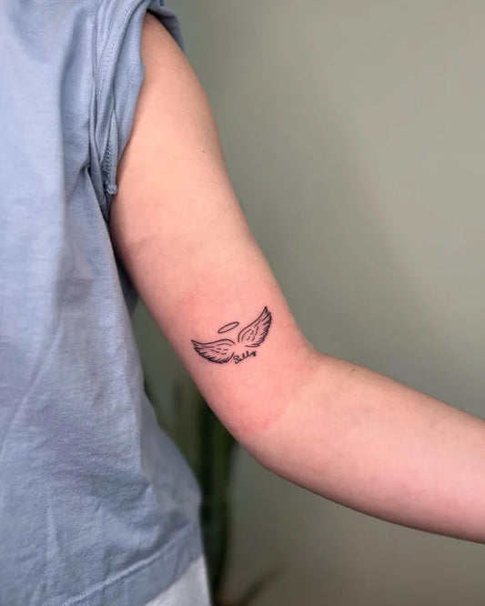 Small Fine Line Angel Wings Tattoo on Women Upper Arm by @lexcreotattoos