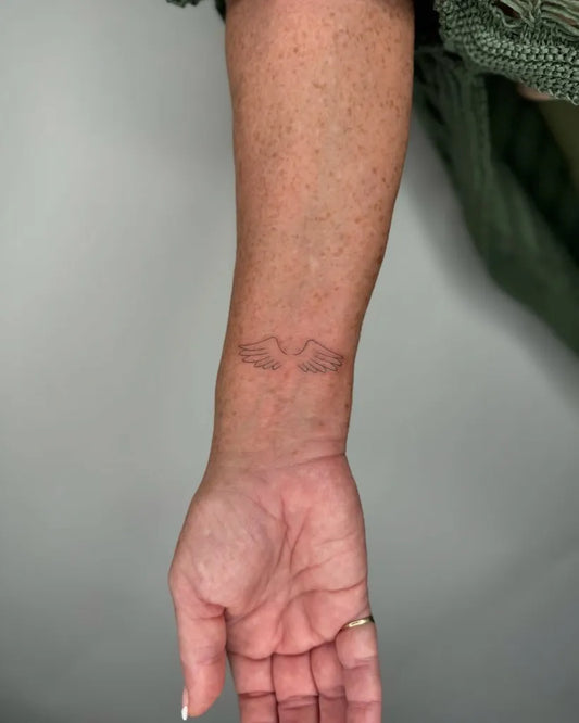 Small Fine Line Angel Wings Tattoo on Women Wrist by @francielitattooart